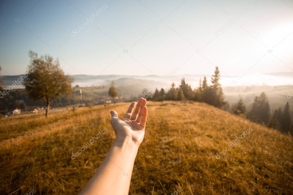 Womans left hand stretches opposite beautiful foggy morning with mountains sunrise