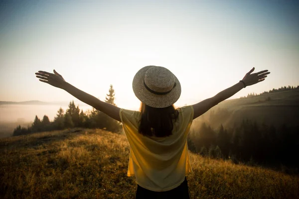 Back view of woman with hands up in straw hat stay outdoor under sunlight of sunrise — Stock Photo, Image