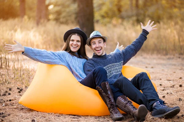 Atractivo sonriente chico y chica en sombrero con las manos arriba divirtiéndose juntos, riendo mientras se pone en el sofá de aire — Foto de Stock