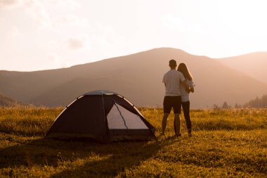 Sırt çantalı genç bir çiftin sonbahar dağlarında gün batımında çadırın yanında yürüyüşünün arkası..
