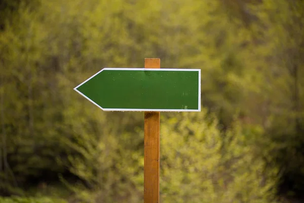 Blank green directional arrow sign on nature background.