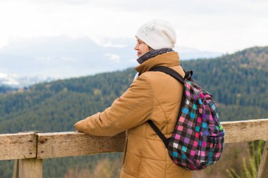 Gözlem güvertesinde duran sırt çantalı ve karla kaplı güzel dağlara bakan mutlu son sınıf öğrencisi kadın.