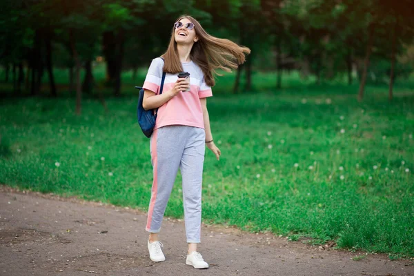 Kawa w drodze. Piękna młoda kobieta w okularach przeciwsłonecznych trzyma kubek kawy i uśmiecha się — Zdjęcie stockowe