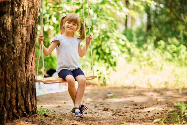 Feliz niña en un columpio en el parque de verano —  Fotos de Stock
