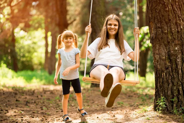 Feliz hija empujando riendo madre en swing en un parque —  Fotos de Stock