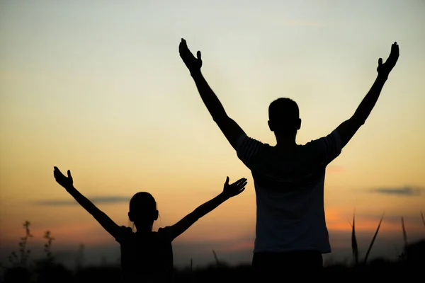 Silhouettes of father and daughter on his shoulders with hands up having fun, against sunset sky. Parenthood, family activities, support and love themes — Stock Photo, Image