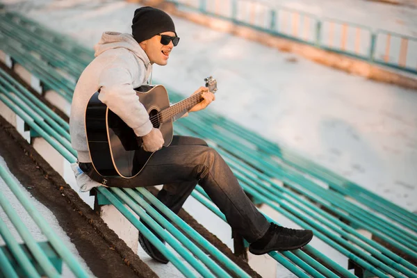 Young man sitting on steps playing guitar and singing, music concept — Stock Photo, Image