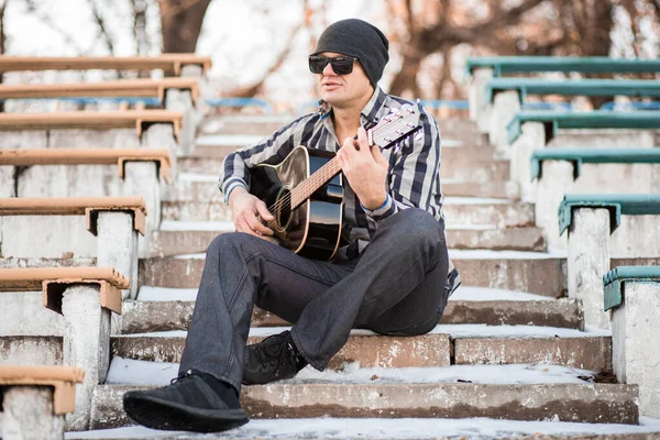 Joven sentado en los escalones tocando la guitarra y cantando, concepto musical — Foto de Stock