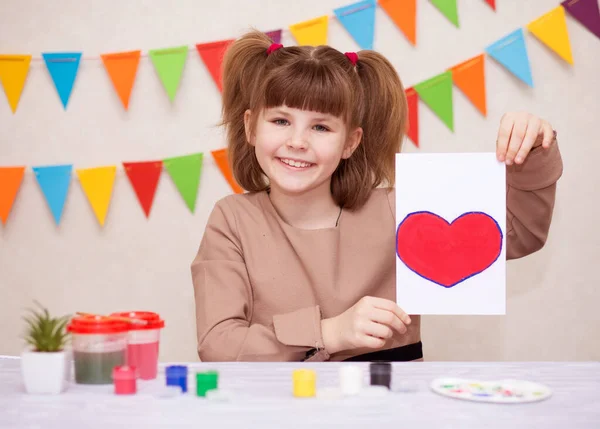 Ребенок делает домашнюю открытку. Маленькая девочка рисует сердце на домашней открытке в качестве подарка на День матери. Традиционная концепция игры. Концепция искусства — стоковое фото
