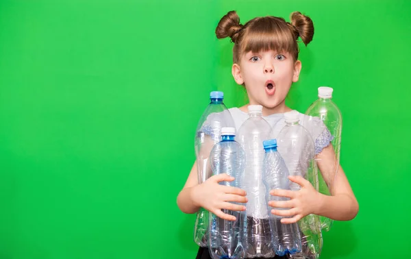 Photo of confused funny little girl holding plastic bottles and looking at camera isolated over green background. ecology concept