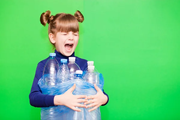 Little girl holding plastic bottles with close eyes and screams for help in protecting our planet from excessive use of plastic isolated on green background