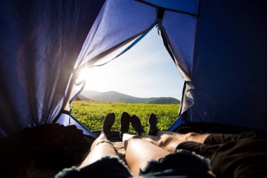 İki kişi çadırda yatıyordu, içeriden bakıyorlardı. Dağların güzel manzaralı günbatımı olan çiftler.