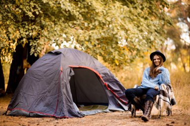 Kamp tatili, kazaklı turist kadın ve ormanda kamp çadırında sallanan siyah şapkalı kadın, yalnız yürüyüşçü kadın doğa yolculuğunun, dinlenme konseptinin tadını çıkar.