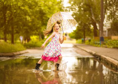 Şemsiye kauçuk çizmeler ve polka nokta elbise ve gülerek su birikintileri üzerinde atlama ile Mutlu komik çocuk kız