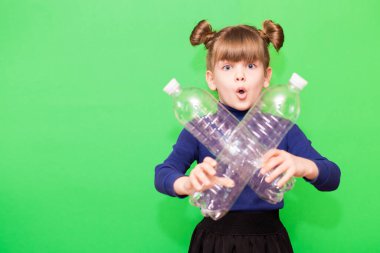 Kafası karışmış, elinde plastik şişelerle yeşil arka planda izole edilmiş küçük bir kızın fotoğrafı.