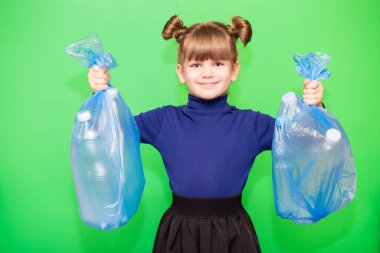Yeşil arka planda plastik şişelerle dolu çöp torbaları tutan pozitif küçük bir çevreci kız. Ekoloji çevre sorunu tüketimi