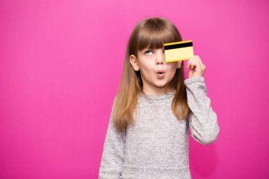 6-7 yaşlarındaki neşeli sarışın utangaç kız kredi kartını pembe arka planda izole etmiş. Çocukluk yaşam tarzı konsepti.