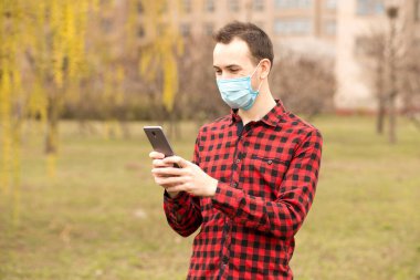 Beyaz adam dışarıda duran virüse karşı gömlek ve koruyucu maske takıyor. İnternet görüntülü mesajlar göndermek için akıllı telefon cep telefonu kullanıyor.