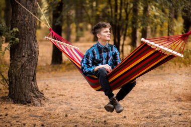 Mavi gömlekli adam hayal kurar ve sonbahar ormanında hamakta dinlenir.