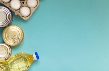 Yiyecek bağışları, yağ şişesi, tavuk yumurtası ve konserve yiyecekler mavi arka planda izole edilmiş.