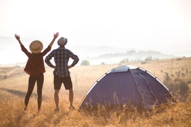 Sevgi dolu çiftin silueti sonbahar tatilinde kamp kurarak rahatlar. Moutain'in üstünde. Eller yukarı ile birlikte gün doğumunun tadını çıkarın.