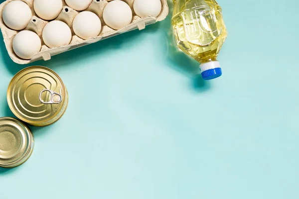 Food product donations, oil bottle, chicken eggs and canned food top view isolated on blue background