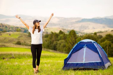 Geceleri dağların tepesinde çadırda güneşe uzanan şapkalı mutlu kadın. Kamp macera konsepti