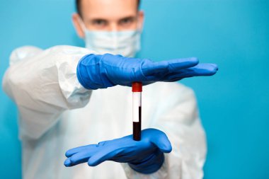 Mavi arka planda izole edilmiş koruyucu maskeli doktor ve eldivenlerde koronavirüs için test edilmiş kan örneği var. Coronavirus COVID 19 için hastaların kanını test ediyoruz..