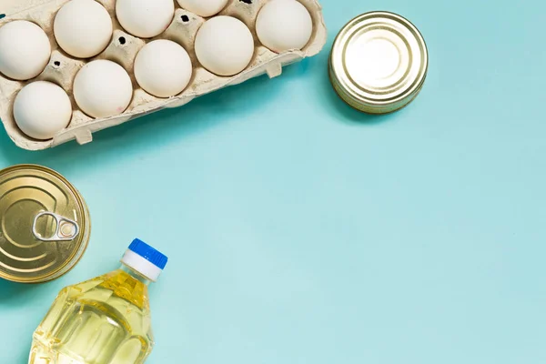 Food product donations, oil bottle, chicken eggs and canned food top view isolated on blue background