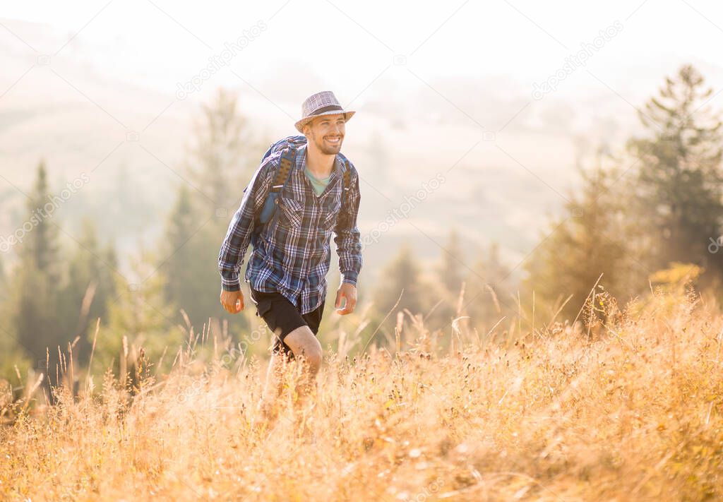 Bearded tourist man in hat with backpack hiking in mountains forest. Caucasian male hiker outdoors in nature.