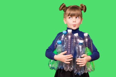 Kafası karışmış, elinde plastik şişelerle yeşil arka planda izole edilmiş küçük bir kızın fotoğrafı. ekoloji kavramı