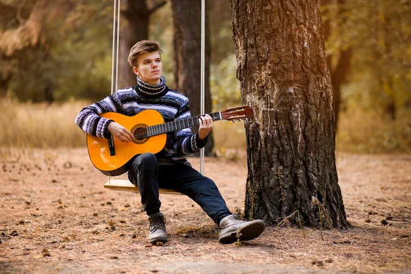 Joven Hombre Atractivo Guapo Suéter Tocando Guitarra Bosque Sentado Swing — Foto de Stock