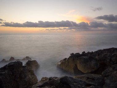 Kayalık kıyılarda dalgaların ezdiği gün batımı