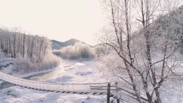 Vue aérienne d'un pont suspendu traversant la rivière dans les Carpates, Ukraine, 4k. Pont couvert de neige. la rivière est légère et rapide — Video