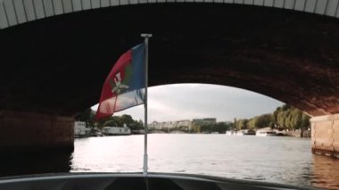 Bir sürat teknesinin kıç tarafında parlayan Fransız bayrağı köprünün altında yüzüyor.