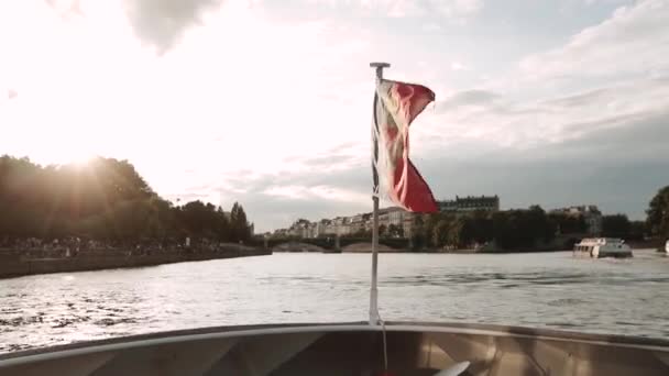 モーターボートの船尾に取り付けられたフランスの旗を振りかける。彼はパリの美しいセーヌ川で泳ぐ。橋は手前にある。. — ストック動画