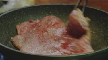 pork steak fry in a frying pan. male hand rotates steak