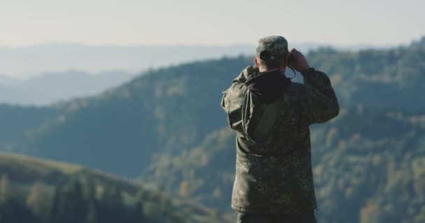 Il cacciatore ha sollevato il binocolo, cercando la sua prossima destinazione in montagna, vista posteriore — Video Stock