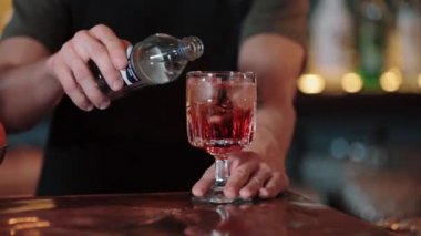Aperol-Spritz kokteyli yapan bir miksologun yavaş çekim videosu. Bir kokteylin içine su döküyor.