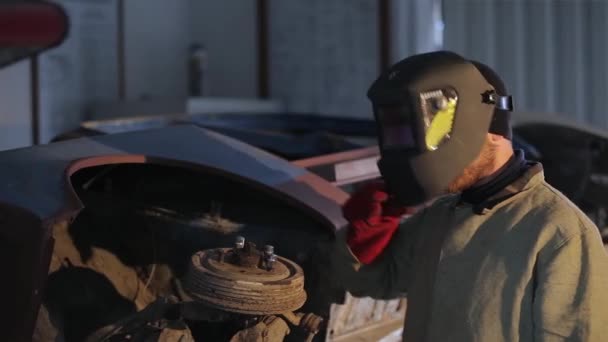 De lasser werkt in de fabriek. machine reparatie. Lassen, helm, felle vonk lassen. Hij kijkt in de camera. — Stockvideo