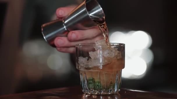 Bartender pours cocktail from measuring cup into ice with mint — Stock Video