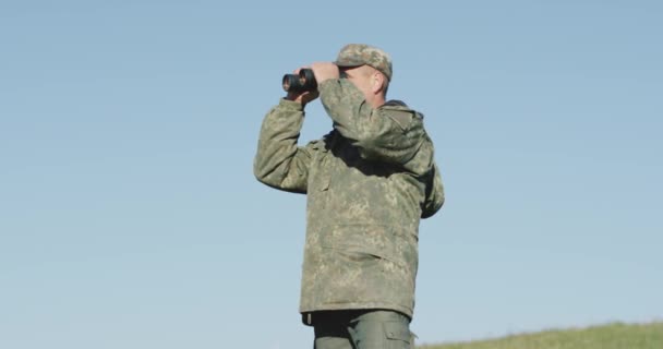 Hunter hief zijn verrekijker, op zoek naar zijn volgende bestemming in de bergen, tegen een blauwe lucht, close-up — Stockvideo