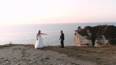 Etretat. Fransa, güzel gelinler doğaya karşı çekilir. Rıhtımda yürüyen genç bir çift. Nazik manzara ve güzel okyanus manzarası. Yavaş çekim.