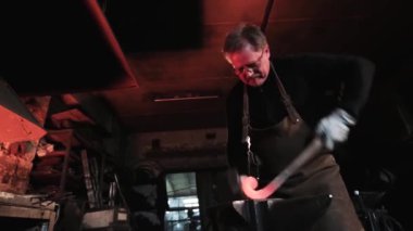 Gözlüklü demirci metal dövmek için çekiç kullanıyor.