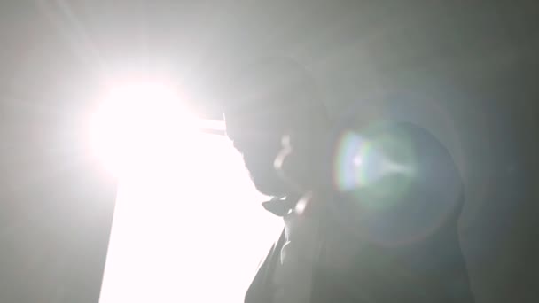 A fiatalember felvesz egy kabátot az ablaknál. Fekete háttér. Egy fénysugár. fénysugár — Stock videók