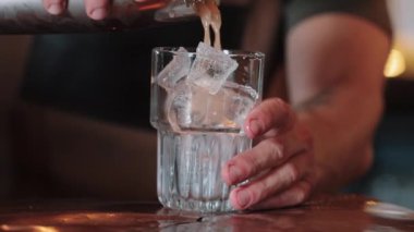 Barmen beyaz kuyruklu tekila kokteylini buzlu bardağa doldurur. Yakın plan.