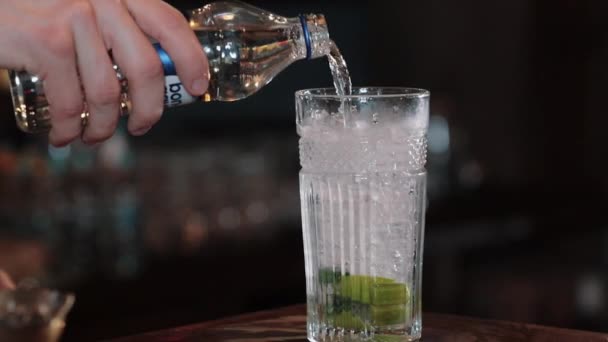 Mojito cocktail making, sparkling water is poured into a glass with mint and lime. close up — Stock Video