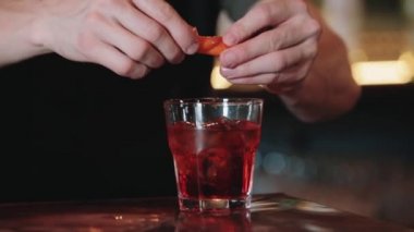Bir barmene yaklaşmak alkollü kokteyl hazırlarken portakal suyu sıkar. Yakın plan. Negroni