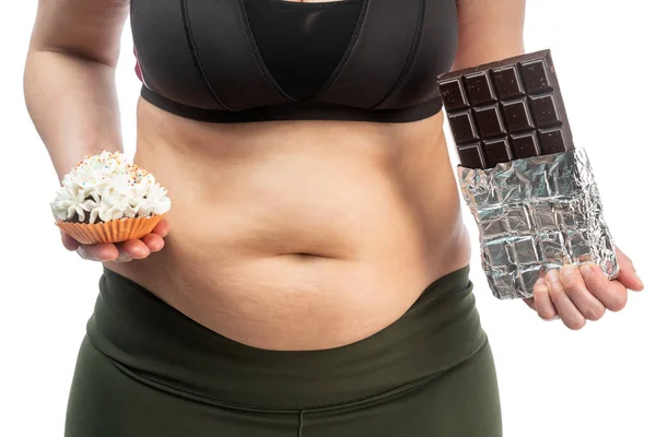 彼女の手にカップケーキとチョコレートで彼女の胃の上に脂肪の折り目を持つ女性 肥満の概念的なイメージ 正面図 — ストック写真