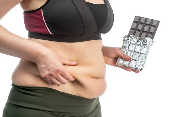 Donna con grasso in eccesso sullo stomaco con il cioccolato in mano. Immagine concettuale dell'obesità. Vista laterale. Isolato su sfondo bianco . — Foto Stock